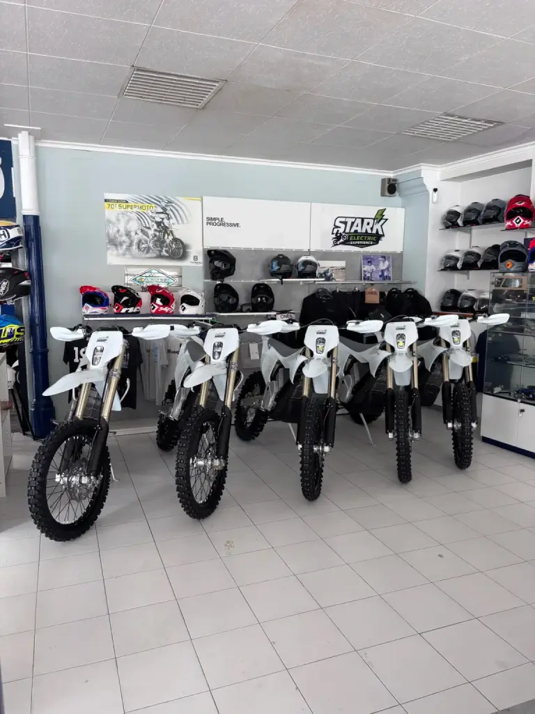 Cinco motos Varg blancas alineadas de frente en la tienda, rodeadas de cascos y equipación.