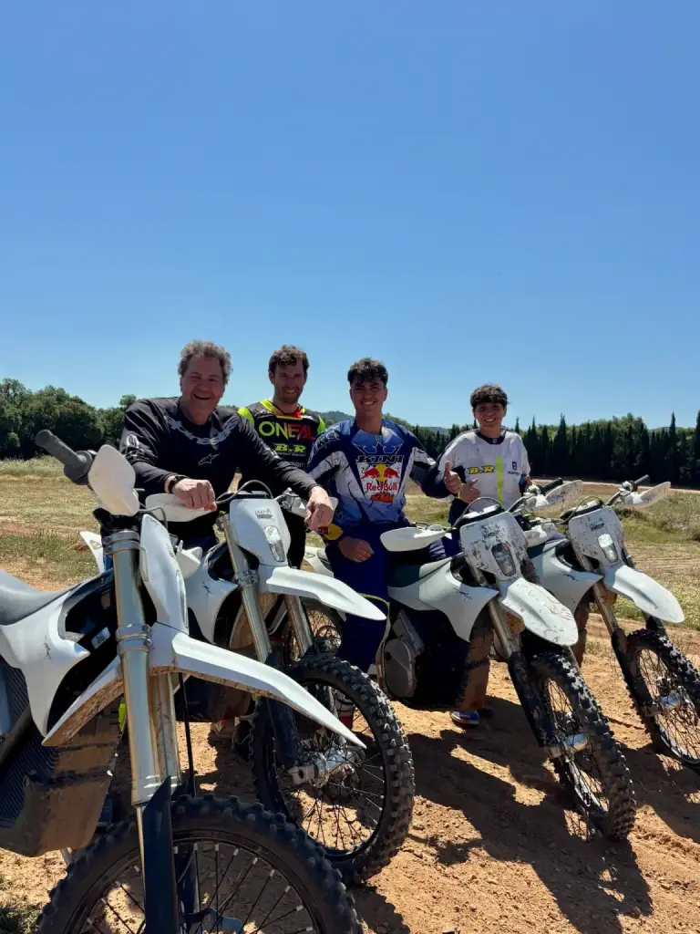 Retrato cercano de cuatro pilotos sonrientes, sin casco, tras sus motos en la pista de tierra.