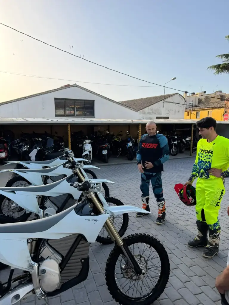 Dos pilotos con equipación charlan junto a la fila de motos eléctricas antes de la salida.